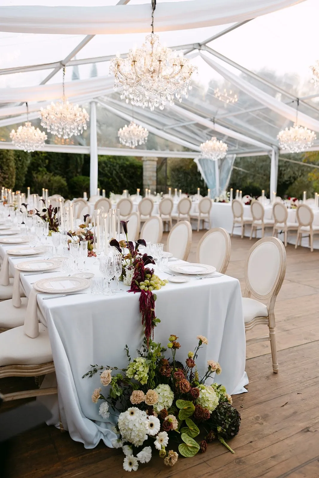 Recepção sob uma tenda com lustres de cristal e mesas longas decoradas com flores